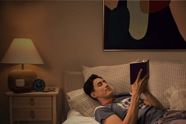 man reclined on sofa reading book under soft lighting