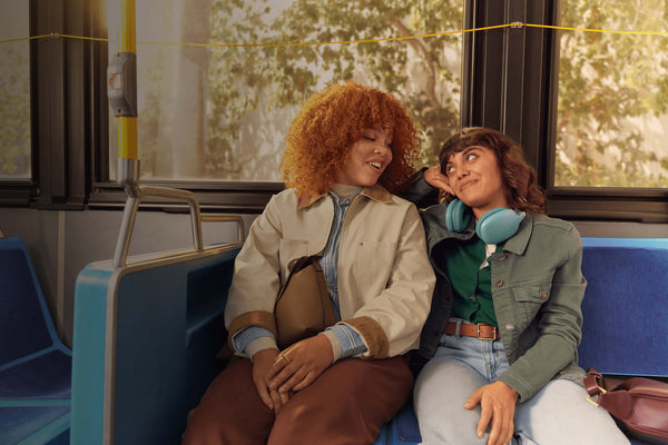 Two women smiling at each other, seated on a bus