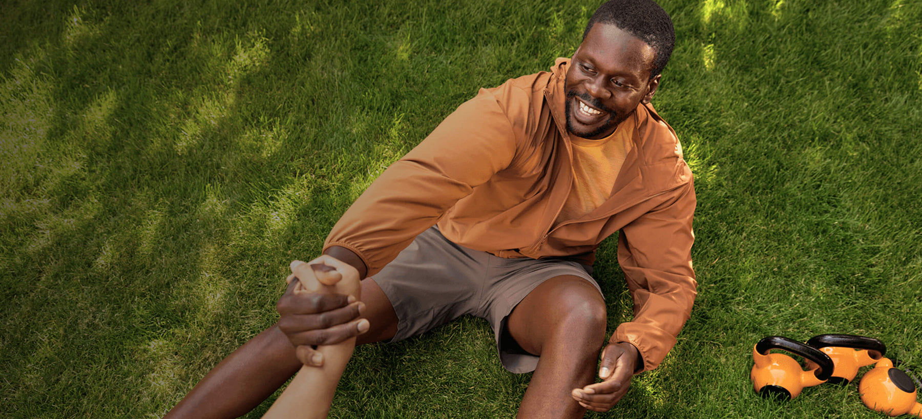 Man sitting on grass beside workout gear, being pulled up by another person