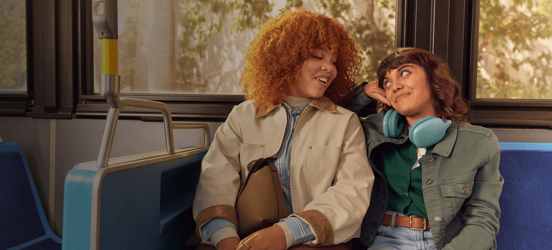 Two women sitting on a bus smiling and looking at each other.