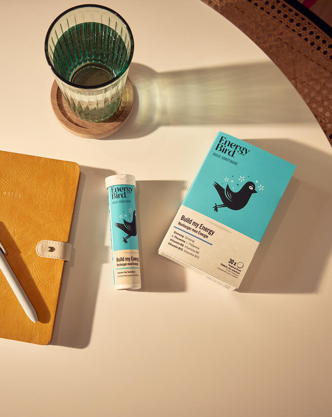 Energy Bird Build My Energy on a yellow table beside a notebook and glass of water