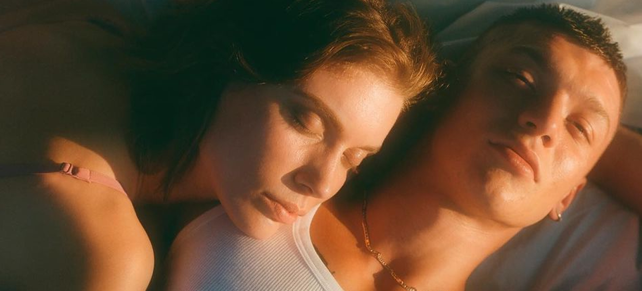 A woman with face on man's chest on a bed in soft lighting.