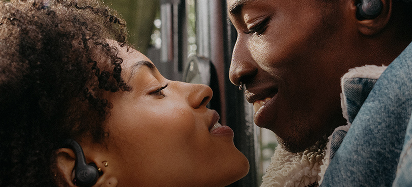 A man and a woman facing each other and smiling and wearing earbuds.