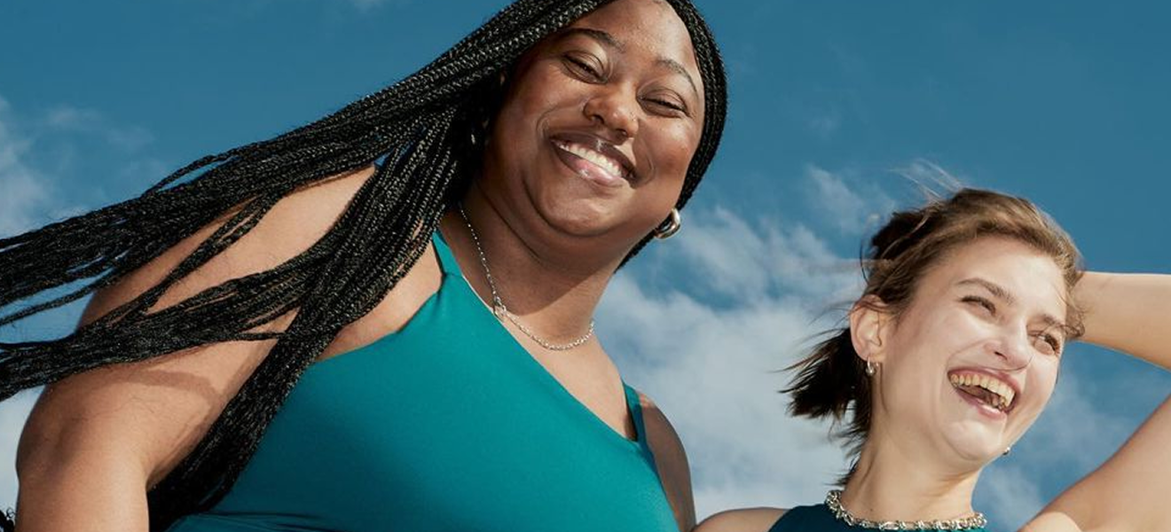 Two women smiling wearing blue clothing in front of a blue sky with white clouds.